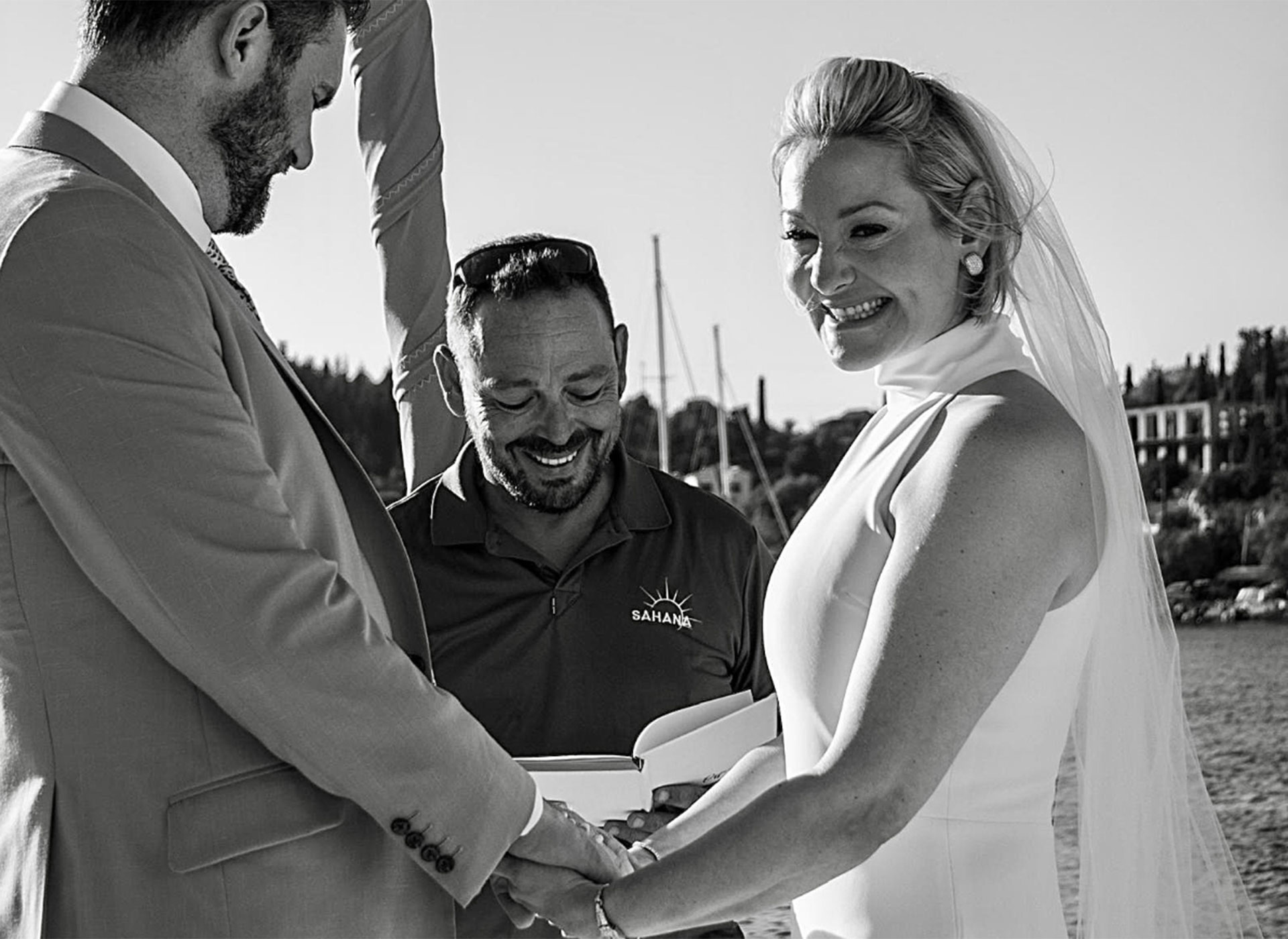 Bride and groom holding hands during yacht charter wedding ceremony with smiling officiant