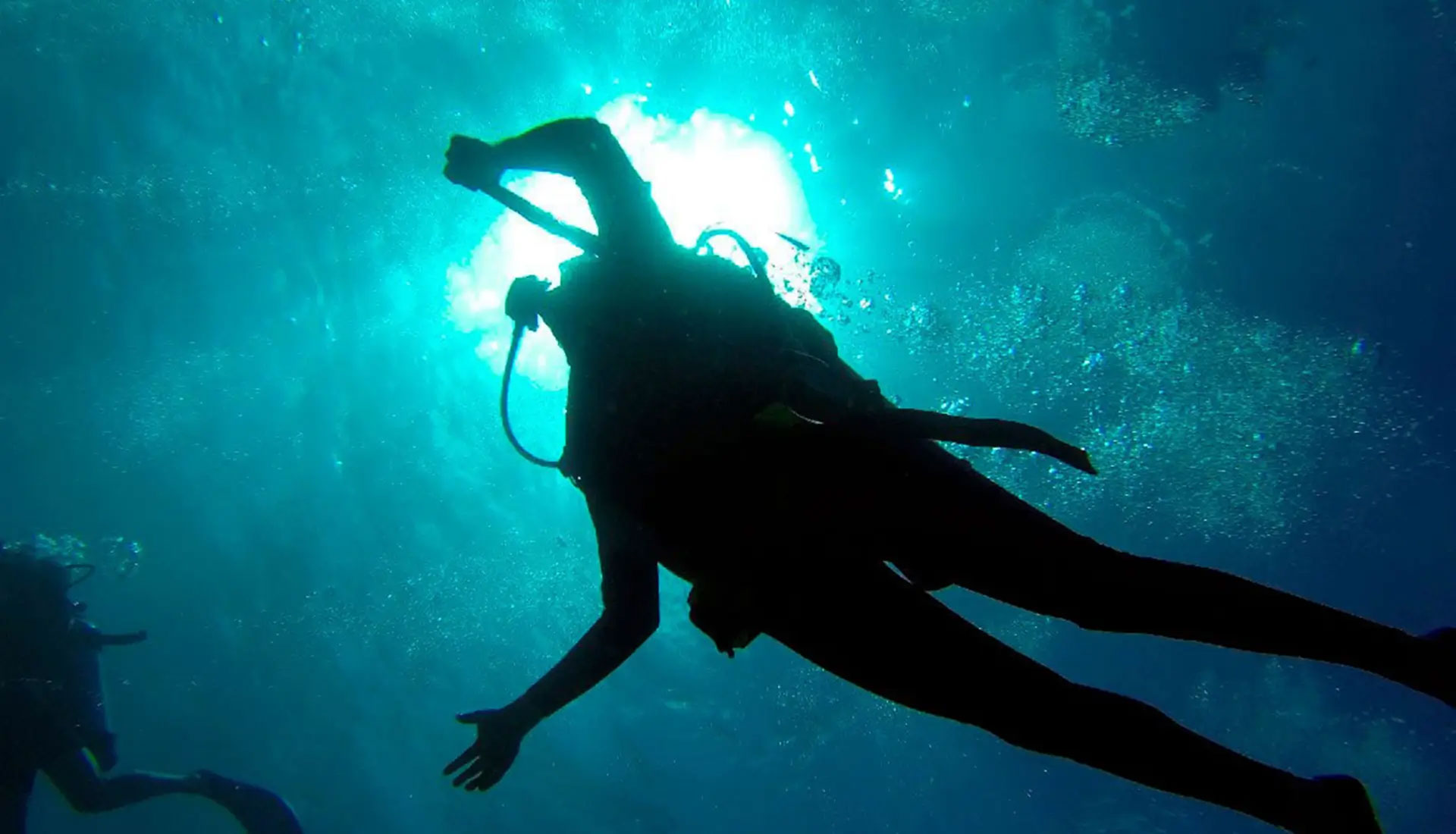 Silhouette of a SCUBA diver exploring underwater with sunlight streaming through the water.