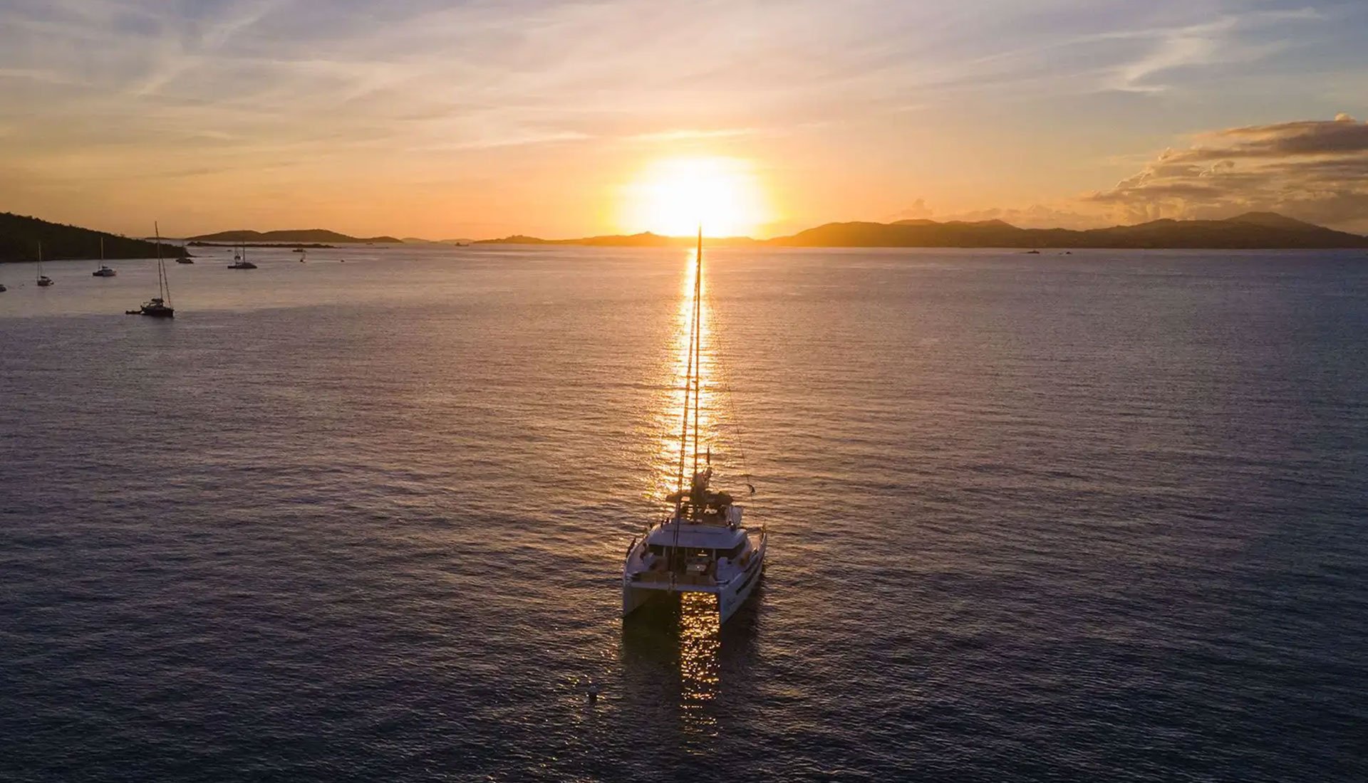 Catamaran anchored at sunset in the British Virgin Islands, with golden light reflecting across the water.