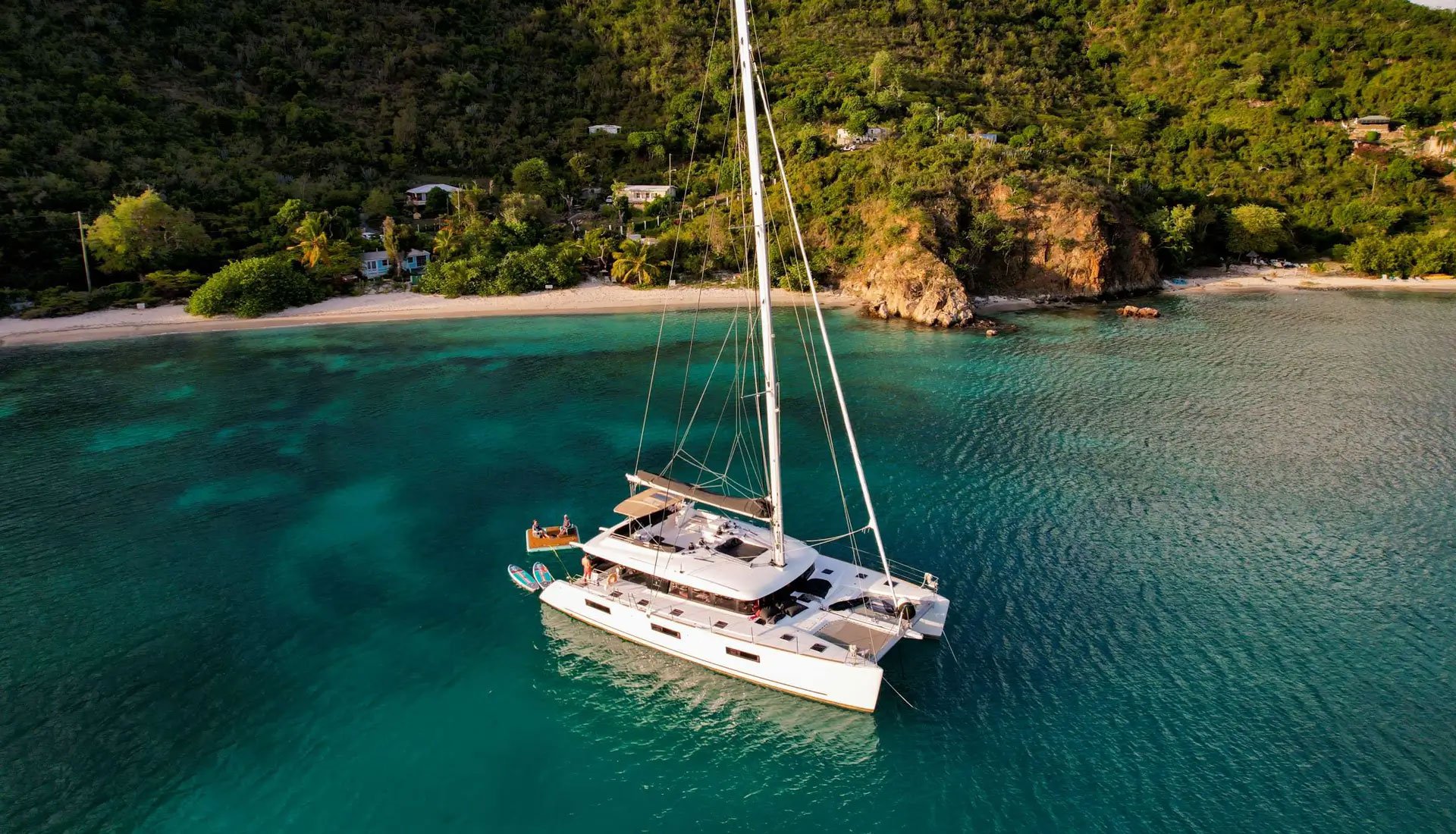 Sailing catamaran anchored in the Virgin Islands with turquoise waters and lush coastline in the background