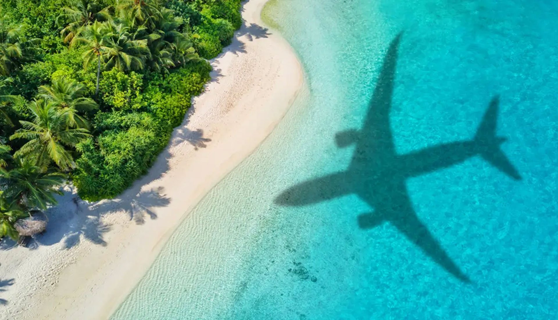 Airplane shadow over turquoise waters and white sand beach in the Virgin Islands, symbolizing arrival for a yacht charter vacation.