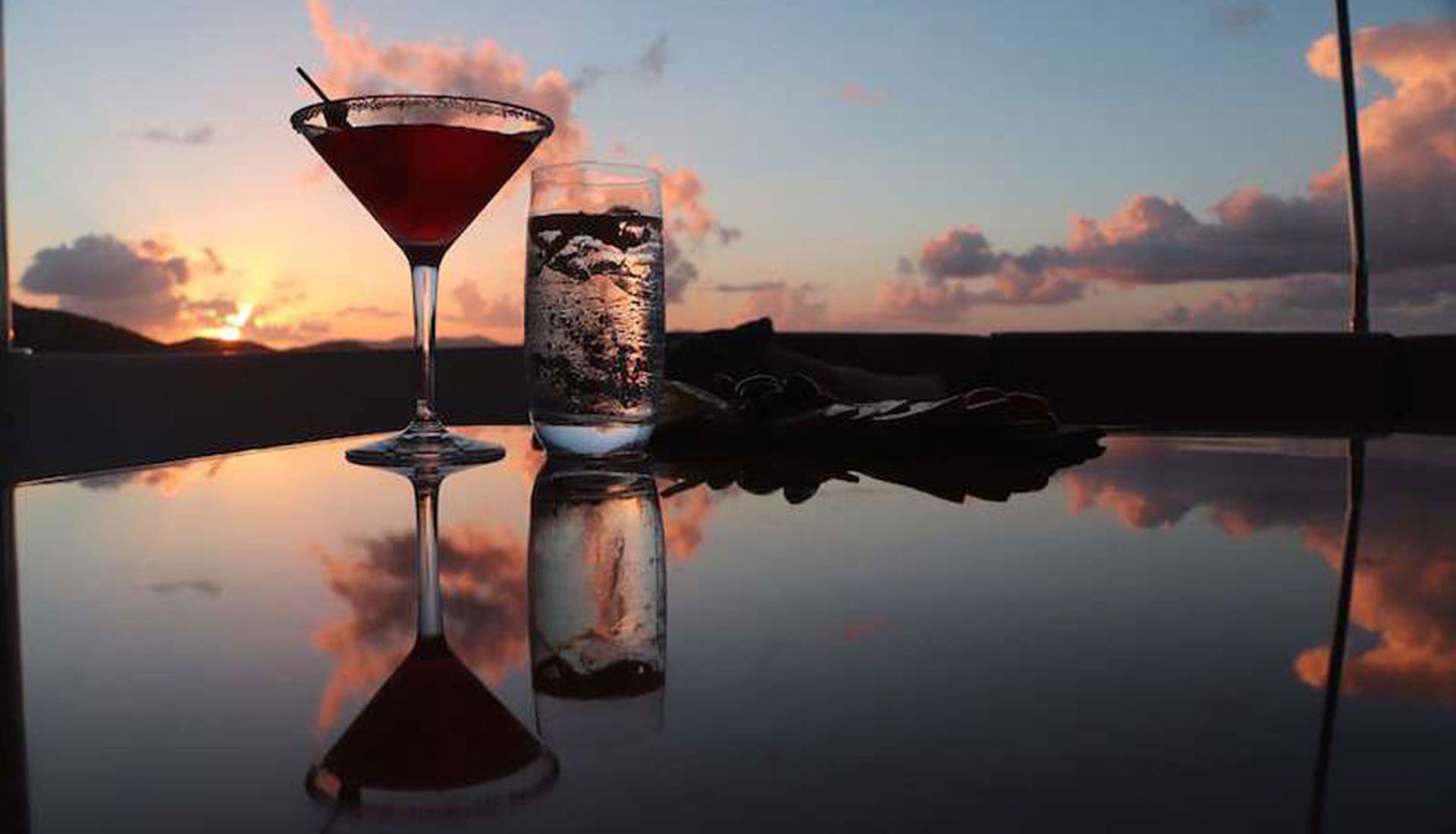 Sunset view with cocktail glass and reflections on a yacht table.