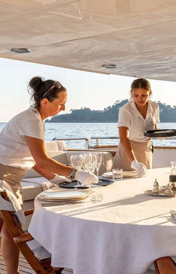 Crew members setting a dining table aboard a luxury yacht, showcasing attentive service during charters.