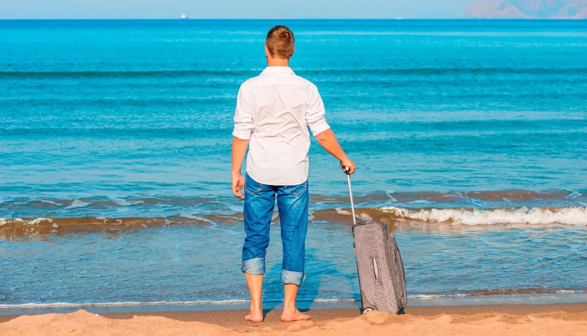 Man standing on the beach with a suitcase, symbolizing arrival and luggage handling for a Caribbean yacht charter.