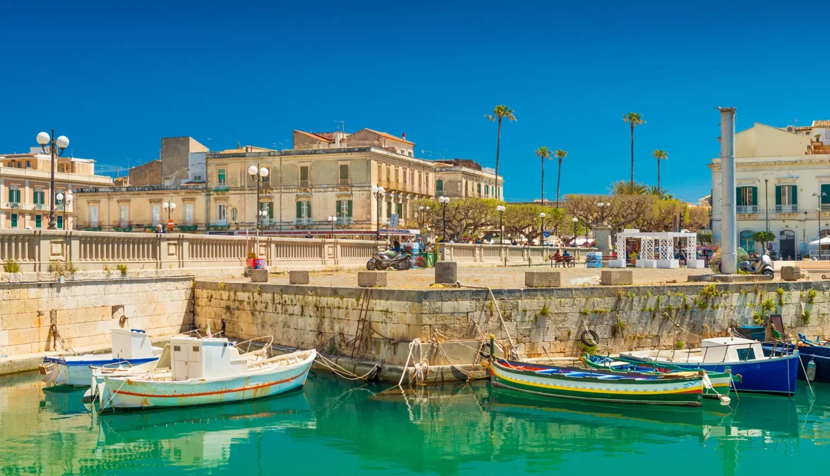 Colorful fishing boats in Syracuse Ortigia harbor with historic baroque buildings Sicily