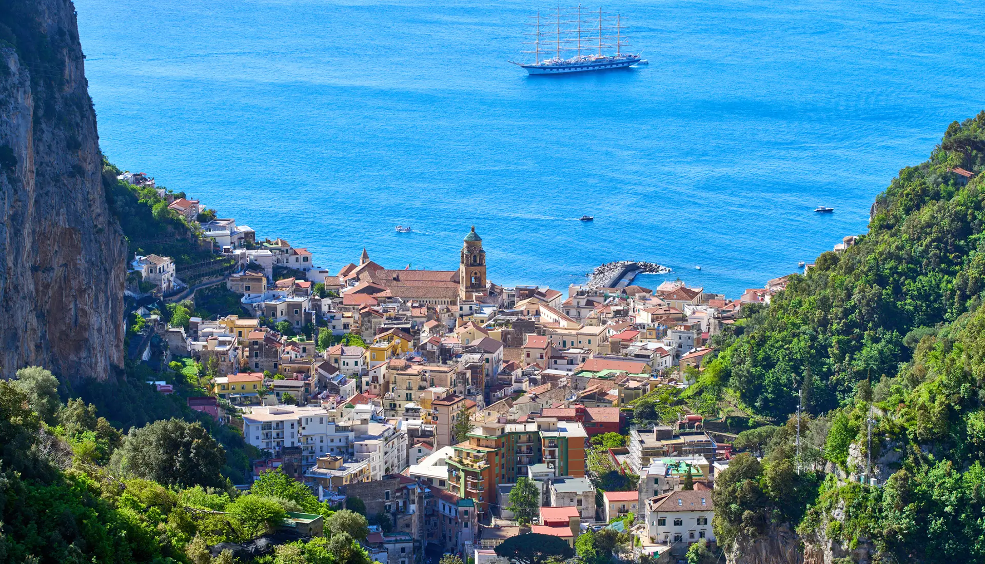 Aerial view of Amalfi town nestled between cliffs with yacht in the Mediterranean Sea