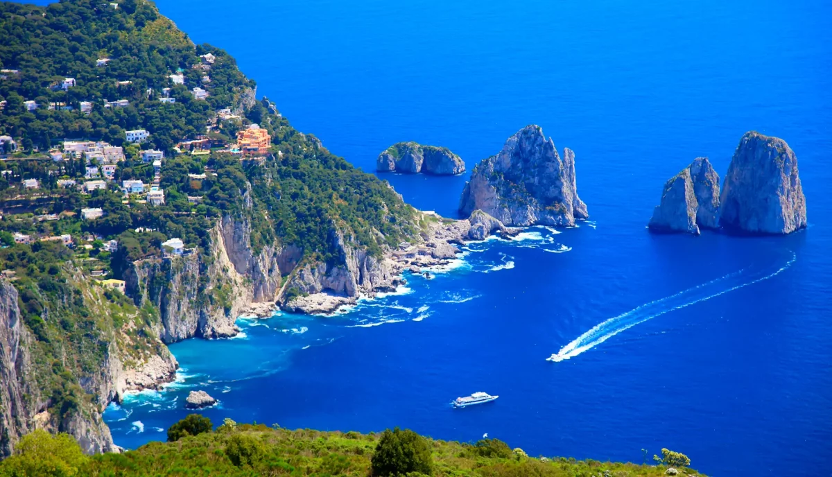 Three Faraglioni rocks of Capri with motor yachts anchored in crystal blue Mediterranean waters