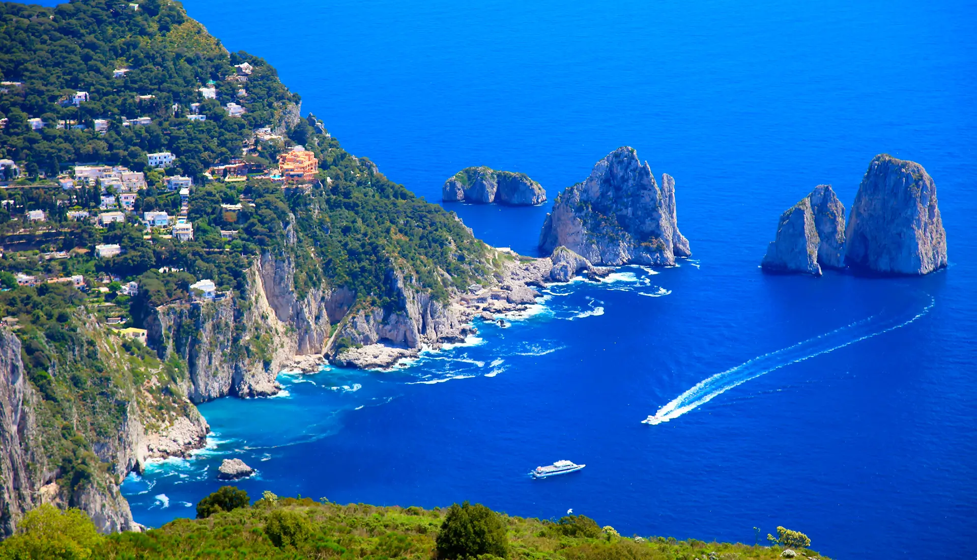 Three Faraglioni rocks of Capri with motor yachts anchored in crystal blue Mediterranean waters