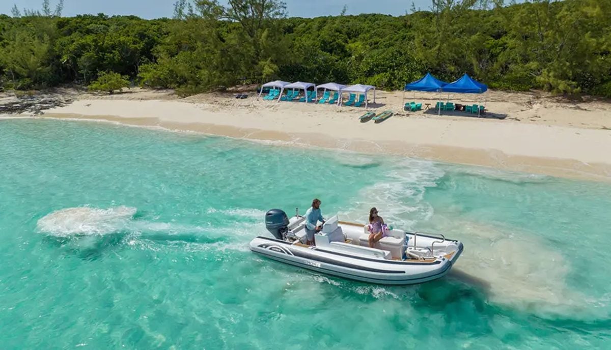 Private beach excursion setup with blue canopy tent and water sports equipment on pristine Caribbean beach with yacht tender in turquoise water