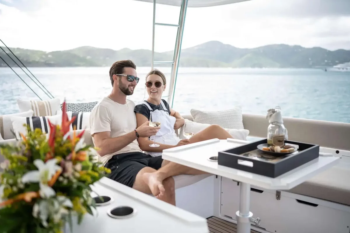 Couple relaxing with wine and appetizers on luxury catamaran flybridge with Caribbean island views