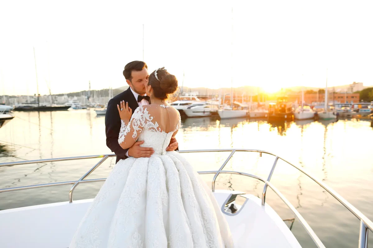 Bride and groom embracing on luxury yacht deck at marina during golden hour sunset wedding ceremony