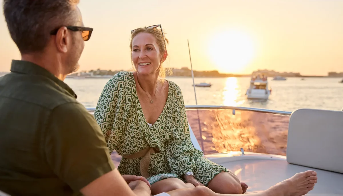 Romantic couple relaxing on luxury yacht charter bow at golden hour sunset with marina background