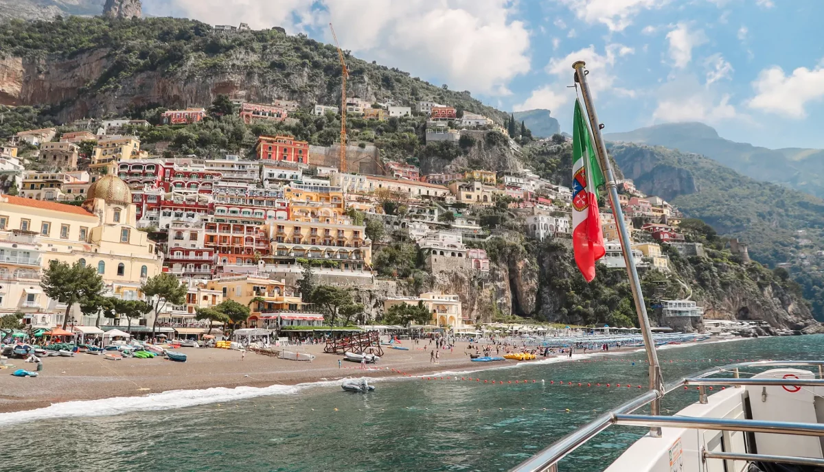 Aerial view of Positano from boat with Italian flag showing colorful houses cascading down Amalfi Coast cliffs