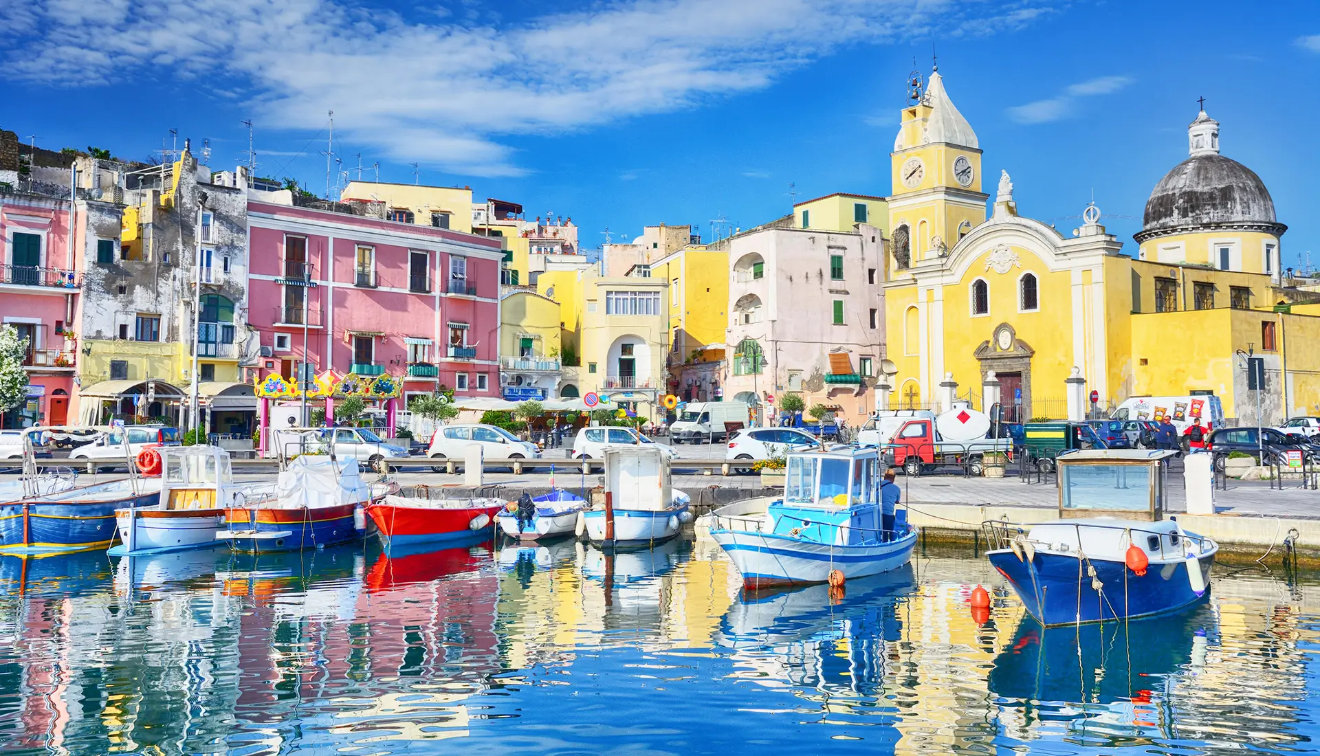 Marina Corricella Procida with colorful houses and church reflected in calm harbor waters