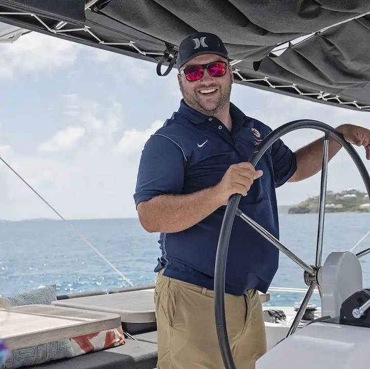 Professional yacht captain at helm steering yacht with guests aboard