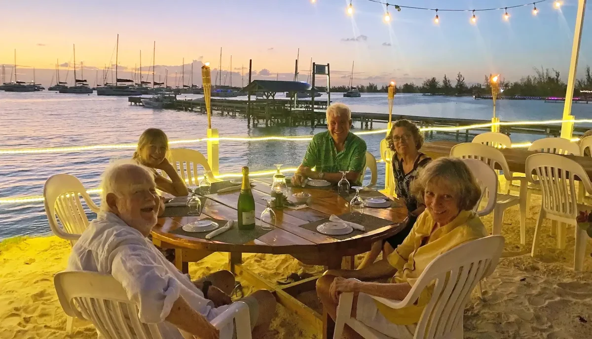 Yacht charter guests dining at beachside restaurant at sunset with yachts anchored in background