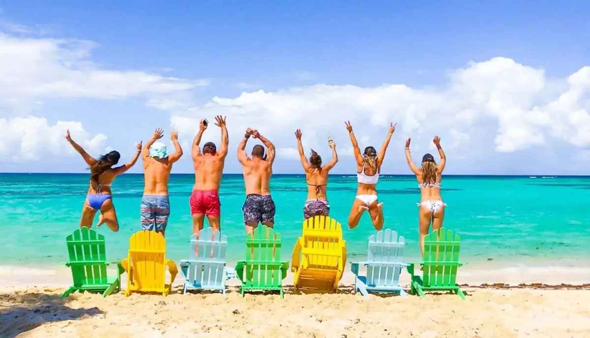 Group of happy yacht charter guests jumping together on Caribbean beach with colorful chairs