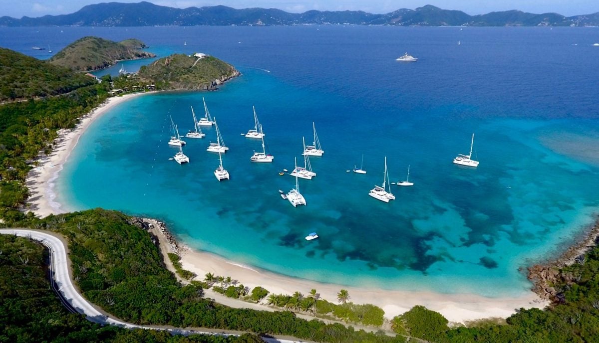Aerial view of Deadman's Bay on Peter Island showing mile-long white sand beach, turquoise water, and charter yachts at anchor in the British Virgin Islands
