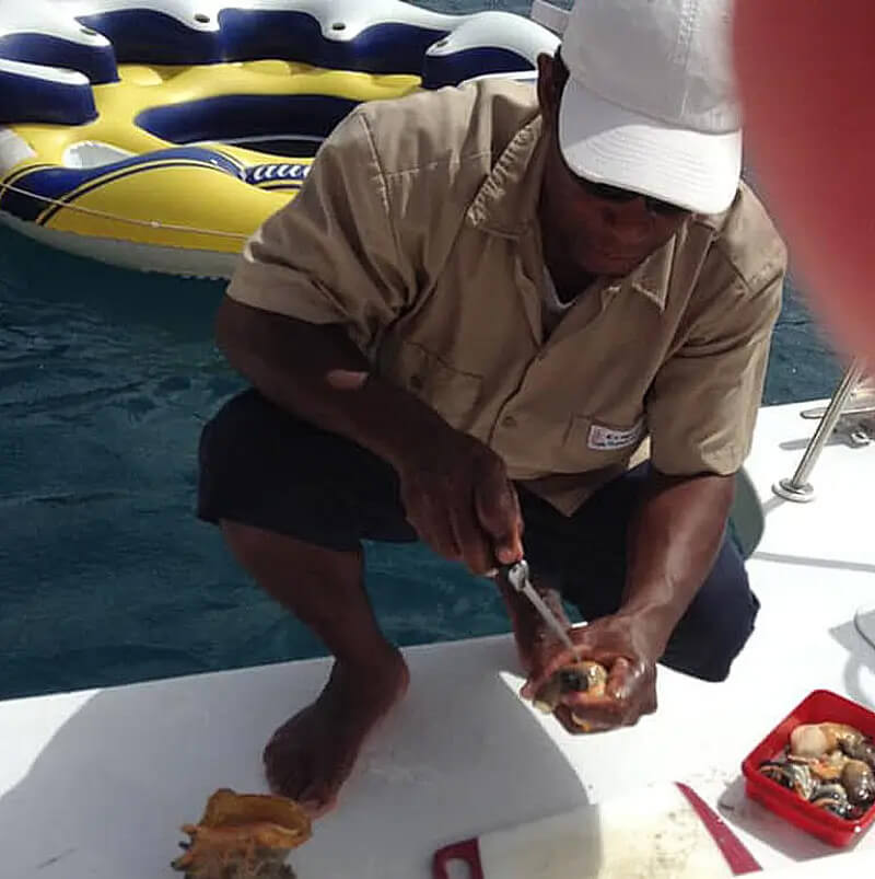 Local BVI fisherman cleaning fresh conch on a boat deck