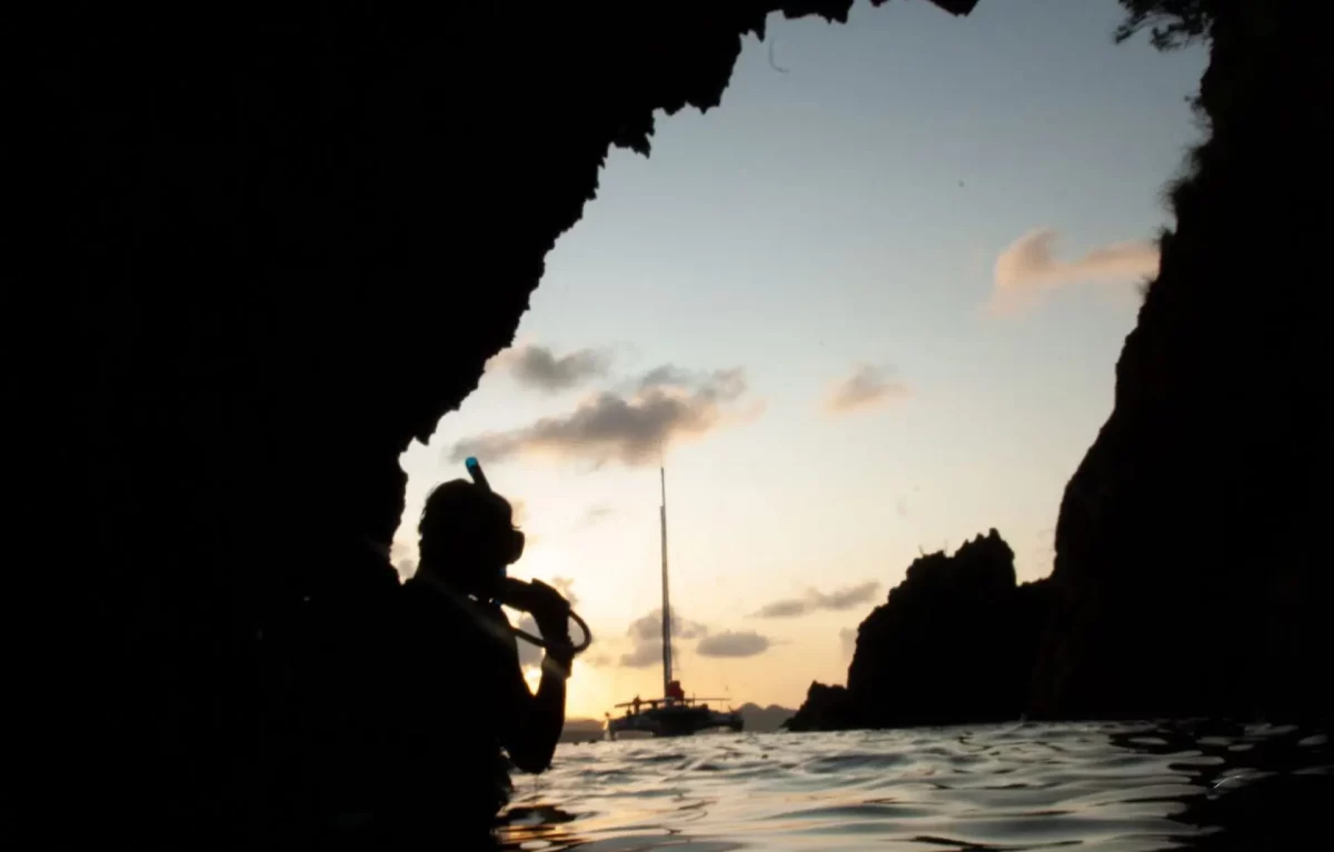 Snorkeler silhouetted inside the Caves at Norman Island BVI at sunset with catamaran in background