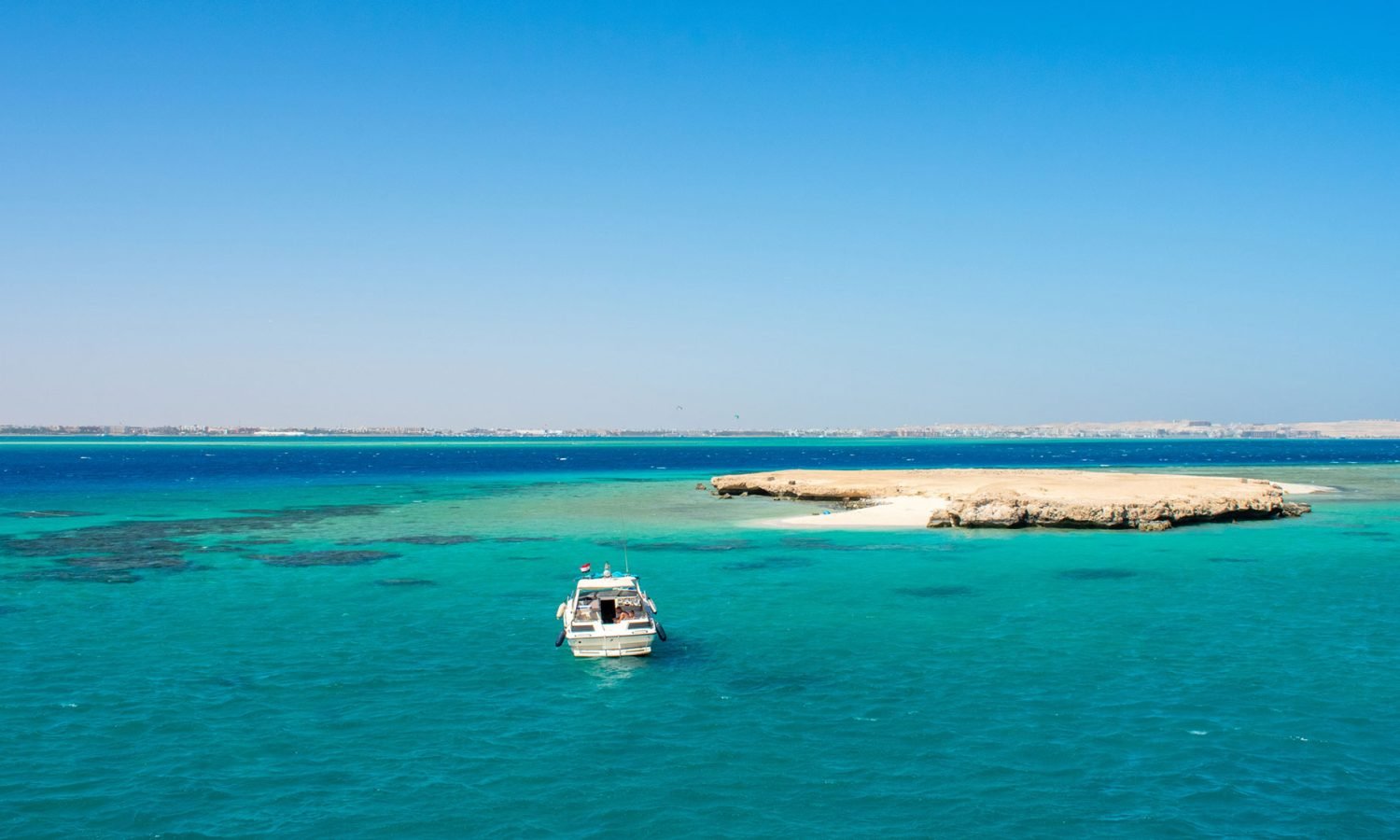 Boat anchored in crystal clear turquoise waters near white sand beach at Tawila Island Red Sea Egypt yacht charter destination