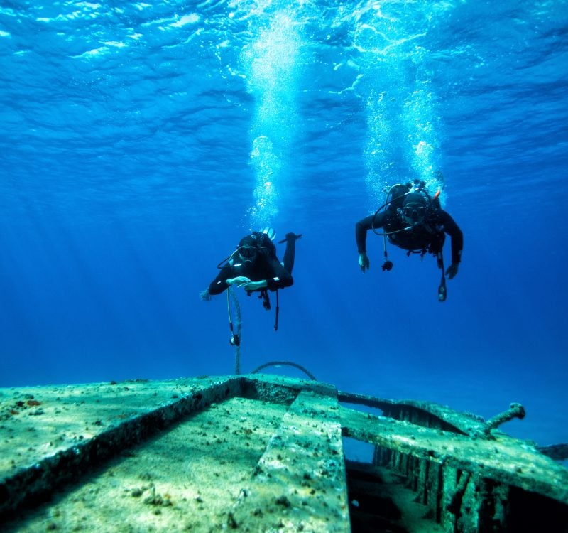 Scuba divers at wreck diving Two scuba divers exploring huge ship wreck on the sand sea bottom.